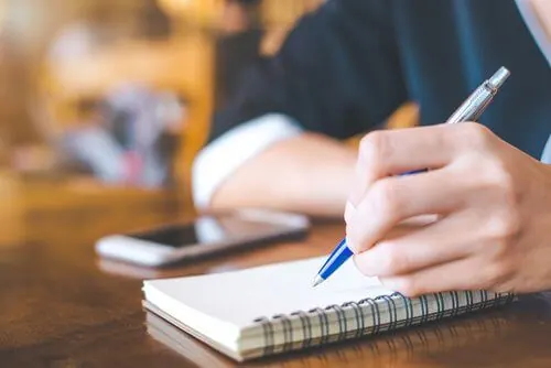 femme prend des notes devant son téléphone
